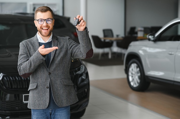 Gelukkige eigenaar van een nieuwe auto Emotionele knappe man in vrijetijdskleding is blij met het kopen van een auto bij de dealer