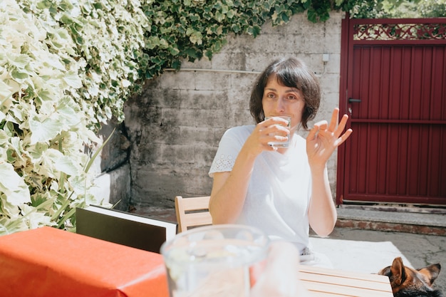 Gelukkige en glimlachende vrouw van middelbare leeftijd die een cadeautje ontvangt tijdens een super zonnige dag in de tuin onder het genot van een drankje