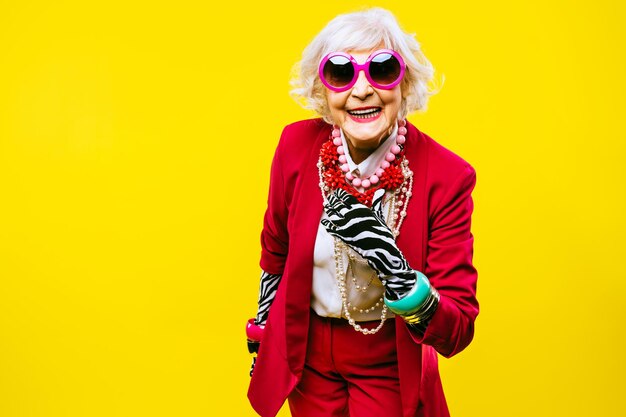 Gelukkige en grappige coole oude dame met modieuze kleding portret op gekleurde achtergrond Jeugdige grootmoeder met extravagante stijlconcepten over levensstijl anciënniteit en ouderen