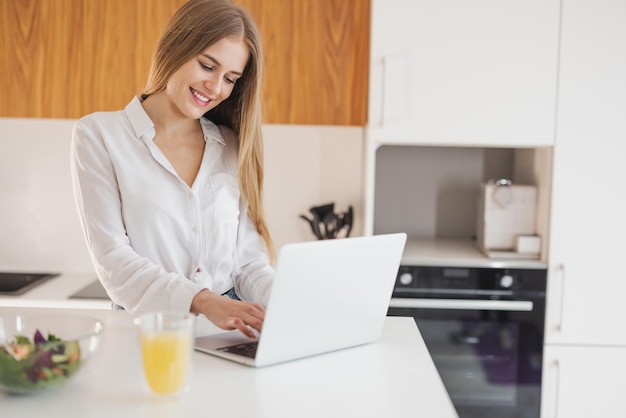 Gelukkige en lachende blonde vrouw op zoek naar recept op laptop op internet in de keuken