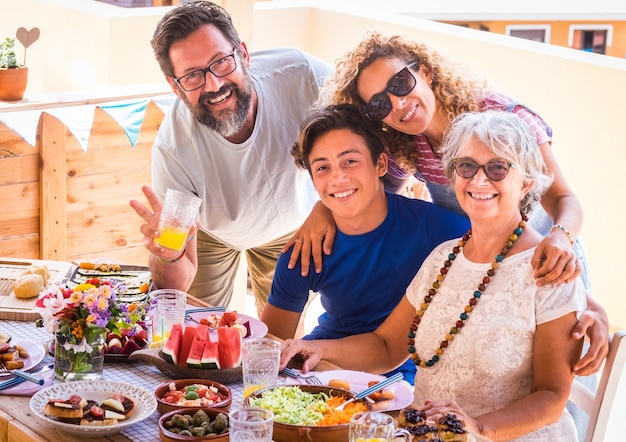 Gelukkige en lachende familie, meerdere generaties. Echtpaar met zoon en oma genieten van brunch of maaltijd samen. Zonlicht op het terrasveld