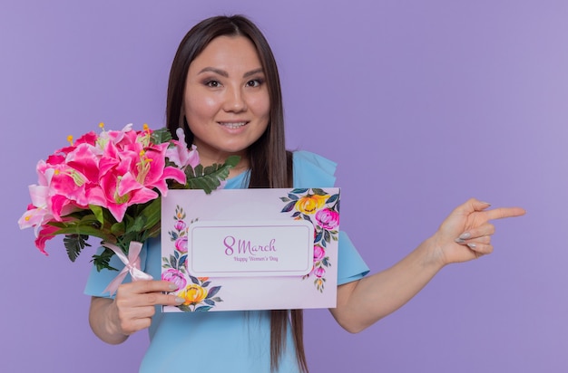 gelukkige en positieve Aziatische vrouw met wenskaart en boeket bloemen