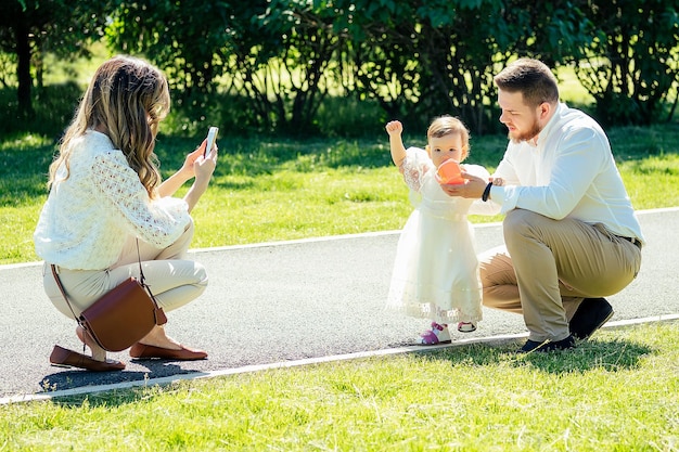 Gelukkige en stijlvolle familie in de zomer in het park. familiefotosessie van mooie moeder, bebaarde vader en schattige dochter die naar de telefoon kijkt