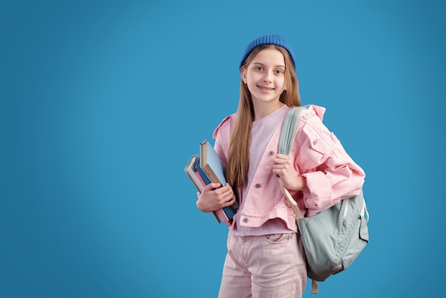 Gelukkige en succesvolle tienerstudent in vrijetijdskleding die rugzak en stapel boeken draagt terwijl hij naar school gaat