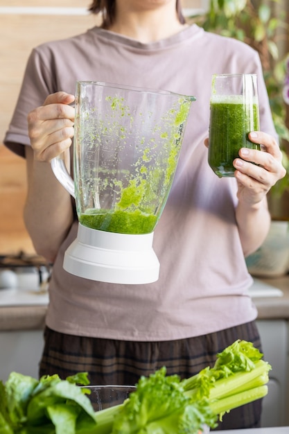 Gelukkige en vrolijke blanke vrouw in een t-shirt in haar keuken maakt een groene smoothie