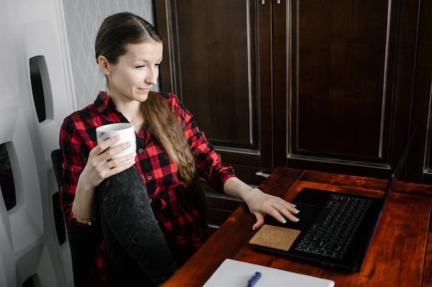 Gelukkige europese vrouwelijke student in casual outfit, glimlachend tijdens het gebruik van laptop