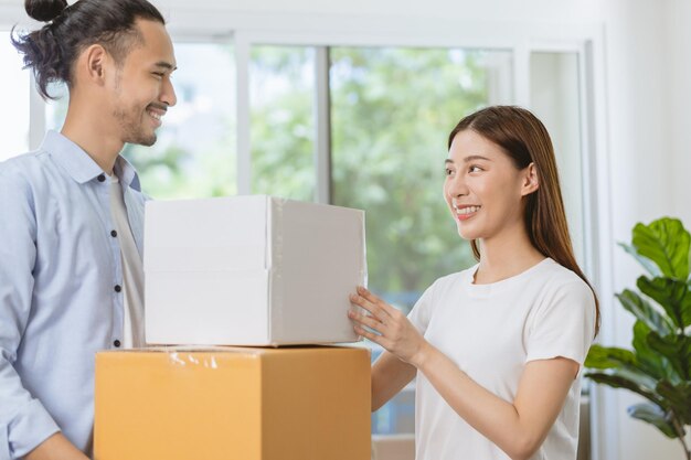 Gelukkige familie aziatische jonge vrouw en man of stel houden kartonnen pakket vast, dragen kartonnen doos voor het voorbereiden van verhuizing, nieuw huis, appartement. Hypotheek, onroerend goed, lening voor huiseigenaarconcept