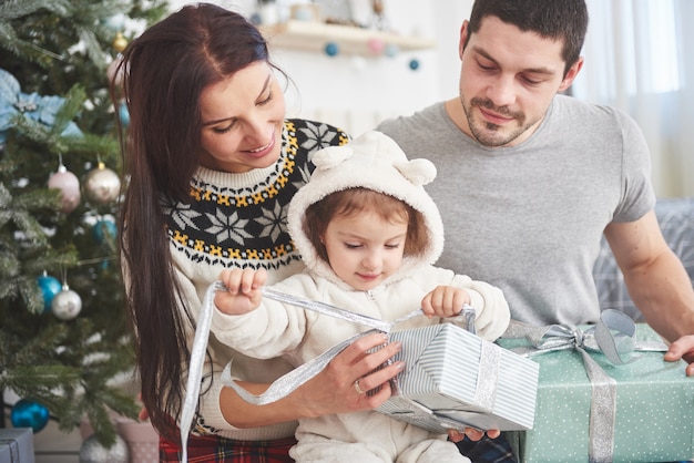 Gelukkige familie bij Kerstmis in ochtend het openen giften samen dichtbij de spar. Het concept van gezinsgeluk en welzijn