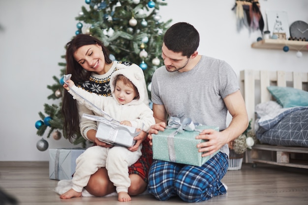 Gelukkige familie bij Kerstmis in ochtend het openen giften samen dichtbij de spar. Het concept van gezinsgeluk en welzijn