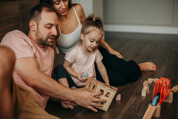 Gelukkige familie brengt tijd samen thuis door met spelen op de vloer met houten speelgoed Jonge brunette vrouw