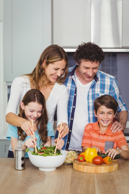 Gelukkige familie die een plantaardige salade voorbereidt