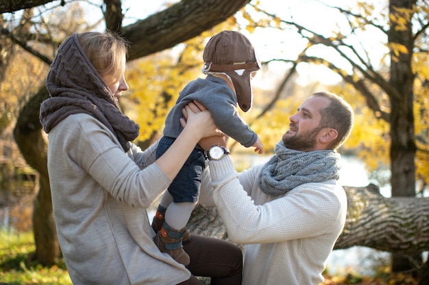 Gelukkige familie die hun klein kind in de herfstpark houden in zonnige dag.