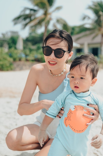 Gelukkige familie die in de zomer op het strand rust, moeder en babyvoeten aan het zeeschuim bij het zonlicht dat water beweegt