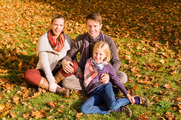 Gelukkige familie die in openlucht op gras in de herfst zit