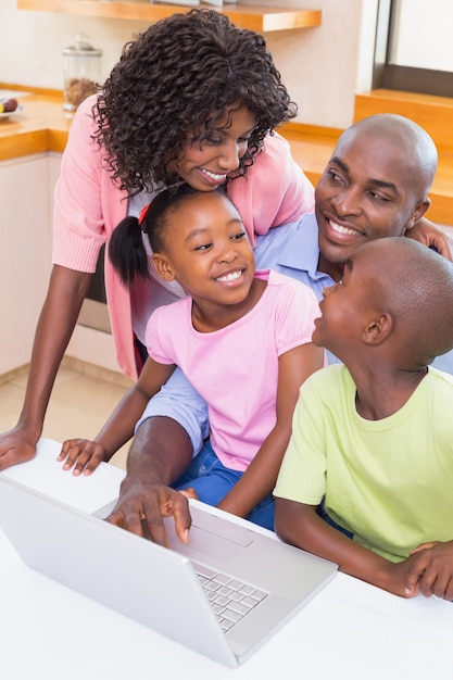 Gelukkige familie die laptop samen thuis in de keuken met behulp van