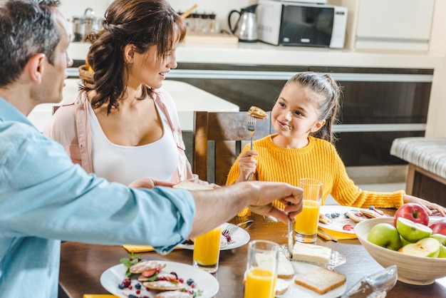 gelukkige familie die pannenkoeken eet aan tafel met sap en fruit in de keuken