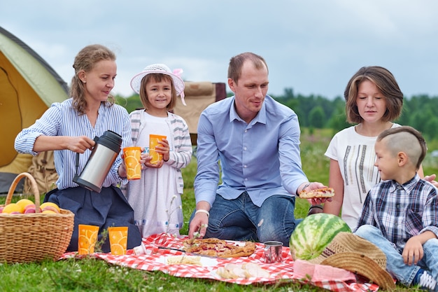 Gelukkige familie die picknick in weide op een zonnige dag heeft. Familie genieten van kampeervakantie op het platteland