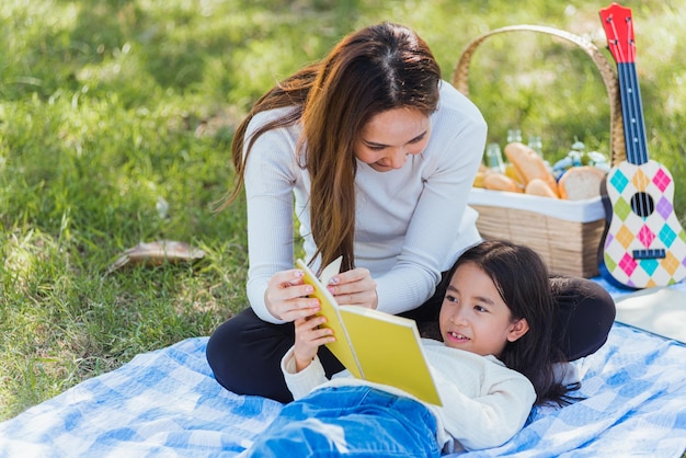 Gelukkige familie die plezier heeft en geniet van het buiten liggend op een picknickdeken leesboek