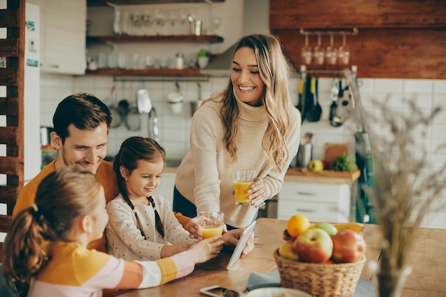 Gelukkige familie die sinaasappelsap drinkt terwijl ze thuis een digitale tablet gebruikt