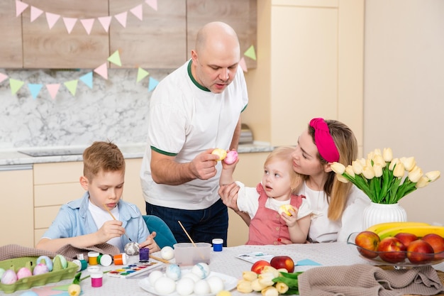 Gelukkige familie die zich voorbereidt op Pasen Schattige kinderen die eieren schilderen Thuisactiviteit Concept van eenheid en liefde Moeder vader zoon dochter Broer en zus