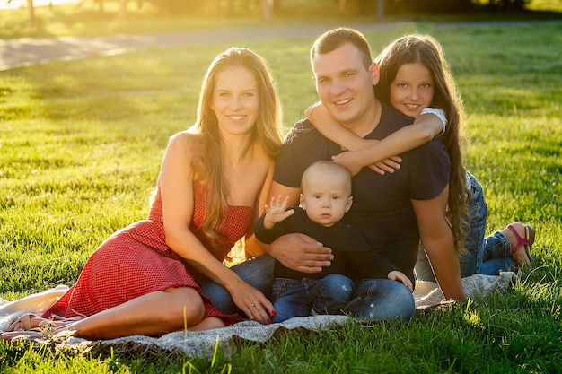 Gelukkige familie fotosessie. mooie moeder vrouw, knappe vader man met een klein meisje dochter schoolmeisje en zoontje van de baby gefotografeerd zittend op het een deken groen gazon park in de zomer.