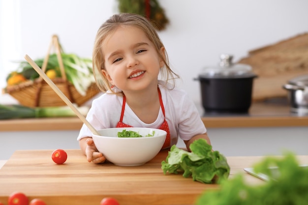 Gelukkige familie in de keuken Moeder en kind dochter koken smakelijk ontbijt van verse salade Kleine helper snijden en mixen van tomaten en groen