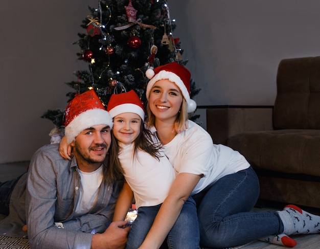 Gelukkige familie in kerstmutsen liggen in de buurt van de kerstboom en glimlachen. Familie traditie.