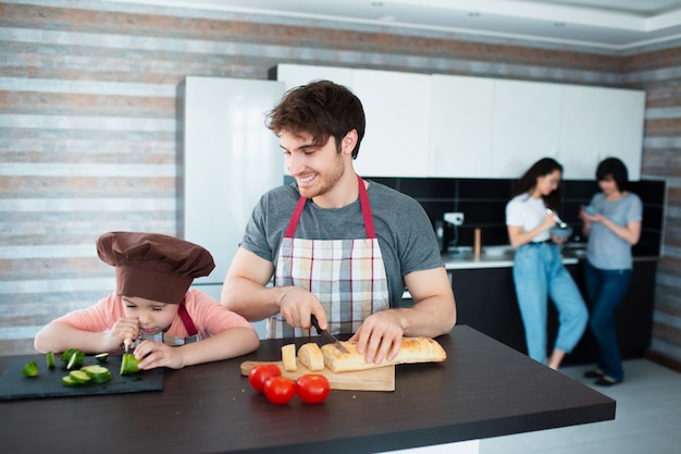 Gelukkige familie is koken in de keuken. Vader leert dochter groenten te snijden.