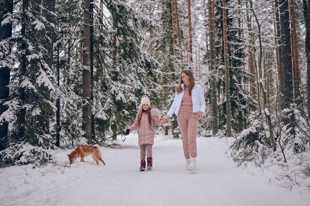 Gelukkige familie jonge moeder en schattig meisje in roze warme uitloper wandelen met plezier met rode shiba inu hond in besneeuwde witte koude winter forest buitenshuis