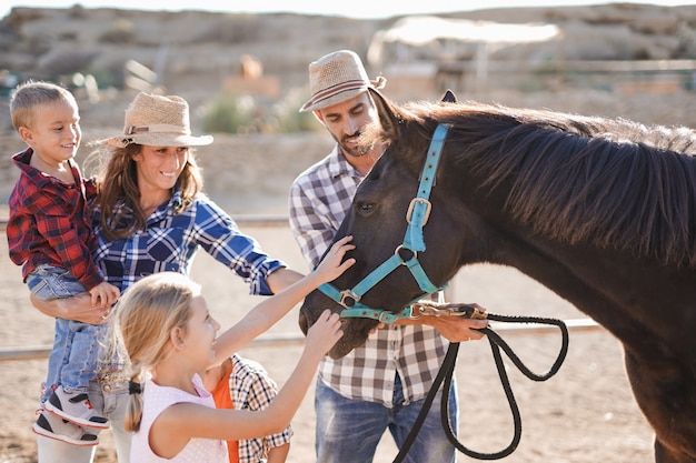 Gelukkige familie knuffel paard op ranch buiten - Dierenliefde en zorgconcept