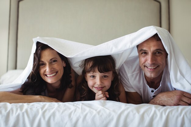 Gelukkige familie liggend onder deken op bed thuis