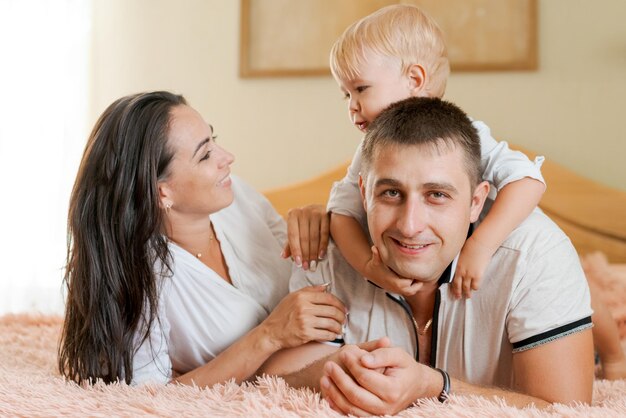 Gelukkige familie liggend op het bed en knuffelen moeder, vader en zoontje