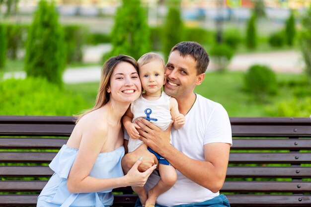 Gelukkige familie mama en papa in het park zittend op een bankje buiten in de open lucht en plezier hebben met een baby in hun armen