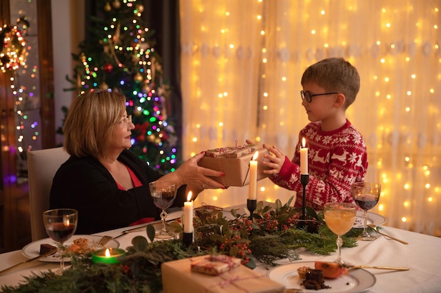 Gelukkige familie met kerstdiner thuis. Kerst vieren met grootouders. Kleinkind dat huidige doos geeft aan grootmoeder.