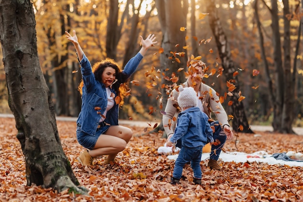 Gelukkige familie met klein schattig kind in park op geel blad met grote pompoen in de herfst