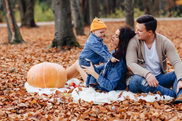 Gelukkige familie met klein schattig kind in park op geel blad met grote pompoen in de herfst