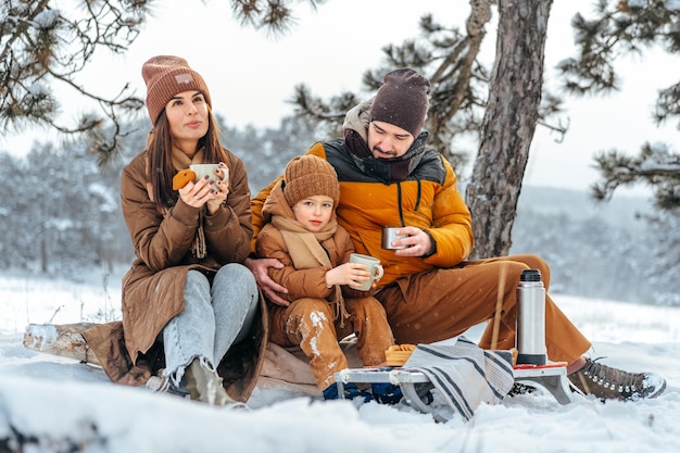 Gelukkige familie met kopjes hete thee tijd samen doorbrengen in winter forest