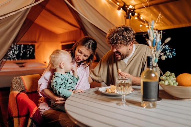 Gelukkige familie met mooie baby dineren en tijd samen doorbrengen in glamping op zomeravond in de buurt van gezellig kampvuur Luxe kampeertent voor openluchtrecreatie en recreatie Lifestyle-concept