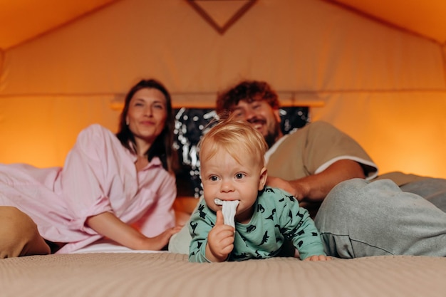 Gelukkige familie met mooie baby spelen en samen tijd doorbrengen in gezellige glamping op zomeravond liggend op bed Luxe kampeertent voor openluchtrecreatie en recreatie