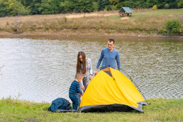 Gelukkige familie met zoontje opgezet camping tent. Gelukkige jeugd, kampeertrip met ouders. Een kind helpt een tent op te zetten