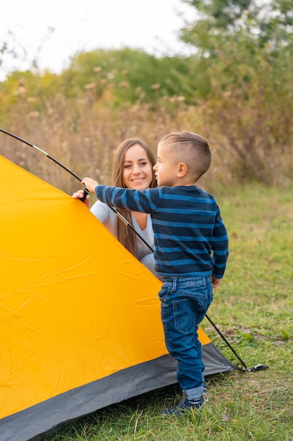 Gelukkige familie met zoontje opgezet camping tent. gelukkige jeugd, kampeertrip met ouders. een kind helpt een tent op te zetten