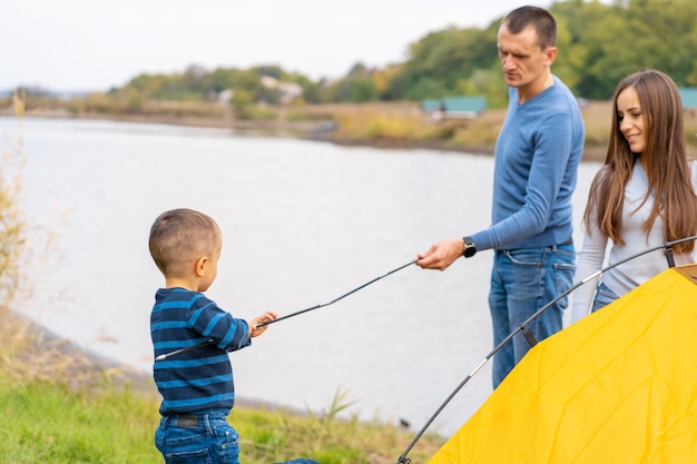 Gelukkige familie met zoontje opgezet camping tent. Gelukkige jeugd, kampeertrip met ouders. Een kind helpt een tent op te zetten