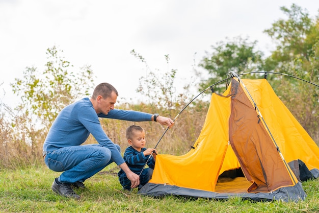 Gelukkige familie met zoontje opgezet camping tent. Gelukkige jeugd, kampeertrip met ouders. Een kind helpt een tent op te zetten