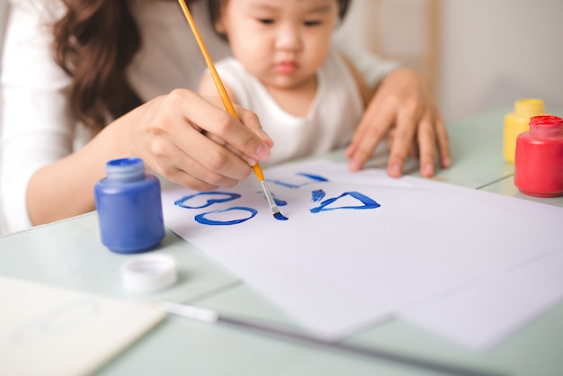 Gelukkige familie moeder en dochter samen schilderen. Aziatische vrouw helpt haar kindmeisje.