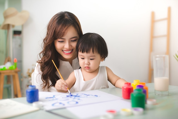 Gelukkige familie moeder en dochter samen schilderen. aziatische vrouw helpt haar kindmeisje.