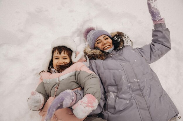 Gelukkige familie moeder en dochter veel plezier met spelen op winterwandeling buiten. moeder en kind liggen in de sneeuw.