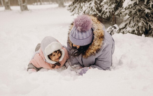 Gelukkige familie moeder en dochter veel plezier met spelen op winterwandeling buiten. moeder en kind liggen in de sneeuw.