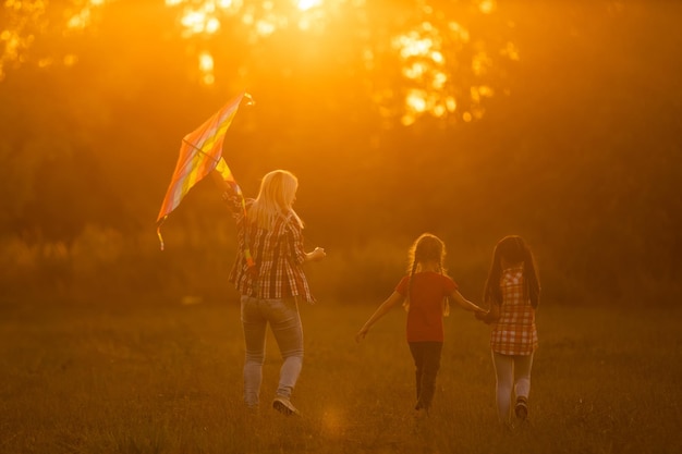 gelukkige familie moeder en kinderen rennen op weide met een vlieger in de zomer op de natuur