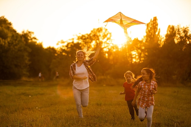 gelukkige familie moeder en kinderen rennen op weide met een vlieger in de zomer op de natuur
