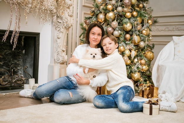 Gelukkige familie moeder en zoon ze zitten in de buurt van een kerstboom met een hond vrouw met familie op kerst...